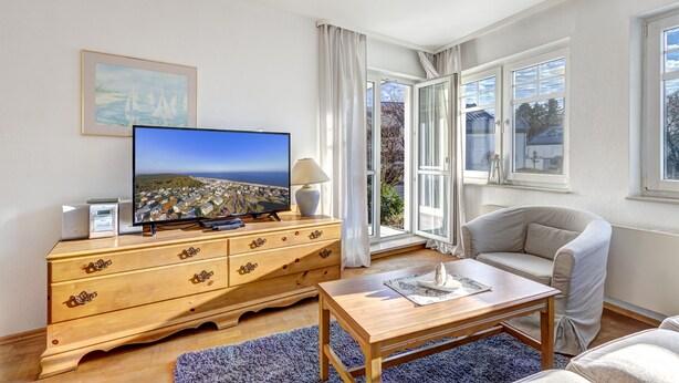 Ein Wohnzimmer mit Fernseher, Holzkommode und einer Couch.
