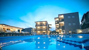 A swimming pool with lounge chairs and a building with multiple balconies. - Royal Hotel and Suites (Kassandra)