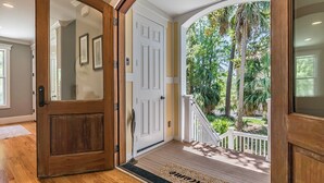 Une porte d’entrée en bois avec un panneau de verre, qui donne sur un porche doté d’une balustrade blanche et d’un paillasson.