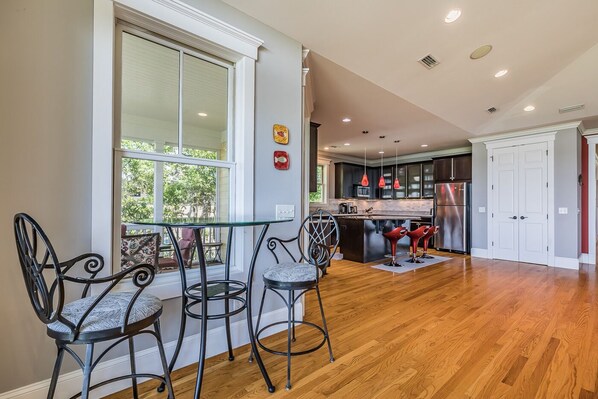 A spacious kitchen with dark cabinets, a stainless steel refrigerator, and a dining area with a glass table and metal chairs. - “What a View!” Pet Friendly - Amazing marsh views, Golf cart included - 160 Davis Love (Fripp Island)