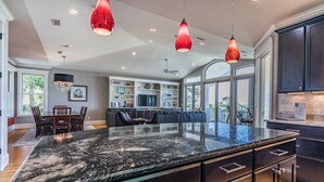 Une cuisine moderne avec des meubles de couleur sombre, un îlot en marbre et des luminaires suspendus.