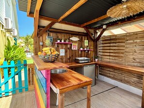 Ein Außenküchenbereich mit einem Holztisch, einer Obstschale und einer Ti-Punch-Bar.