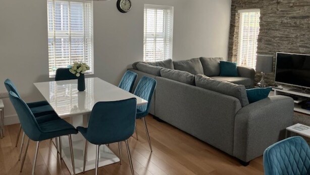 Un salon moderne avec un canapé gris, des fauteuils bleus, une table à manger blanche et un mur d’accent en pierre.