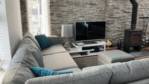 Un salon avec un mur en pierre, un canapé, un téléviseur, une lampe et une cheminée.