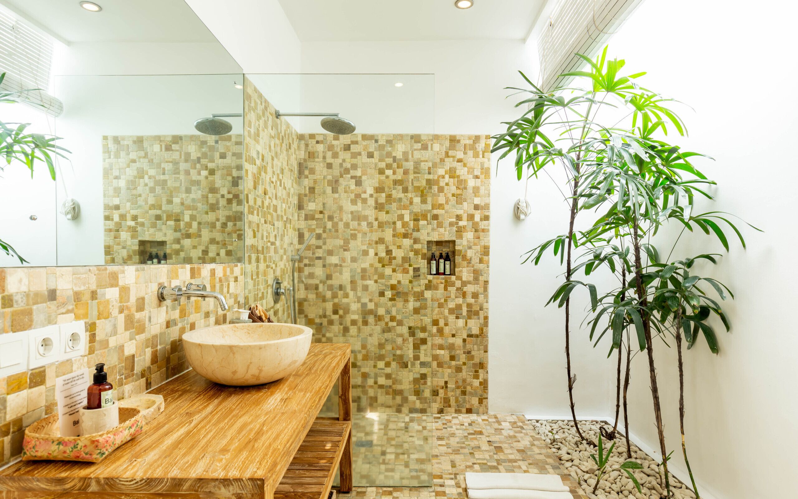 A bathroom with a wooden vanity, a large sink, a shower with a mosaic wall, and several plants.