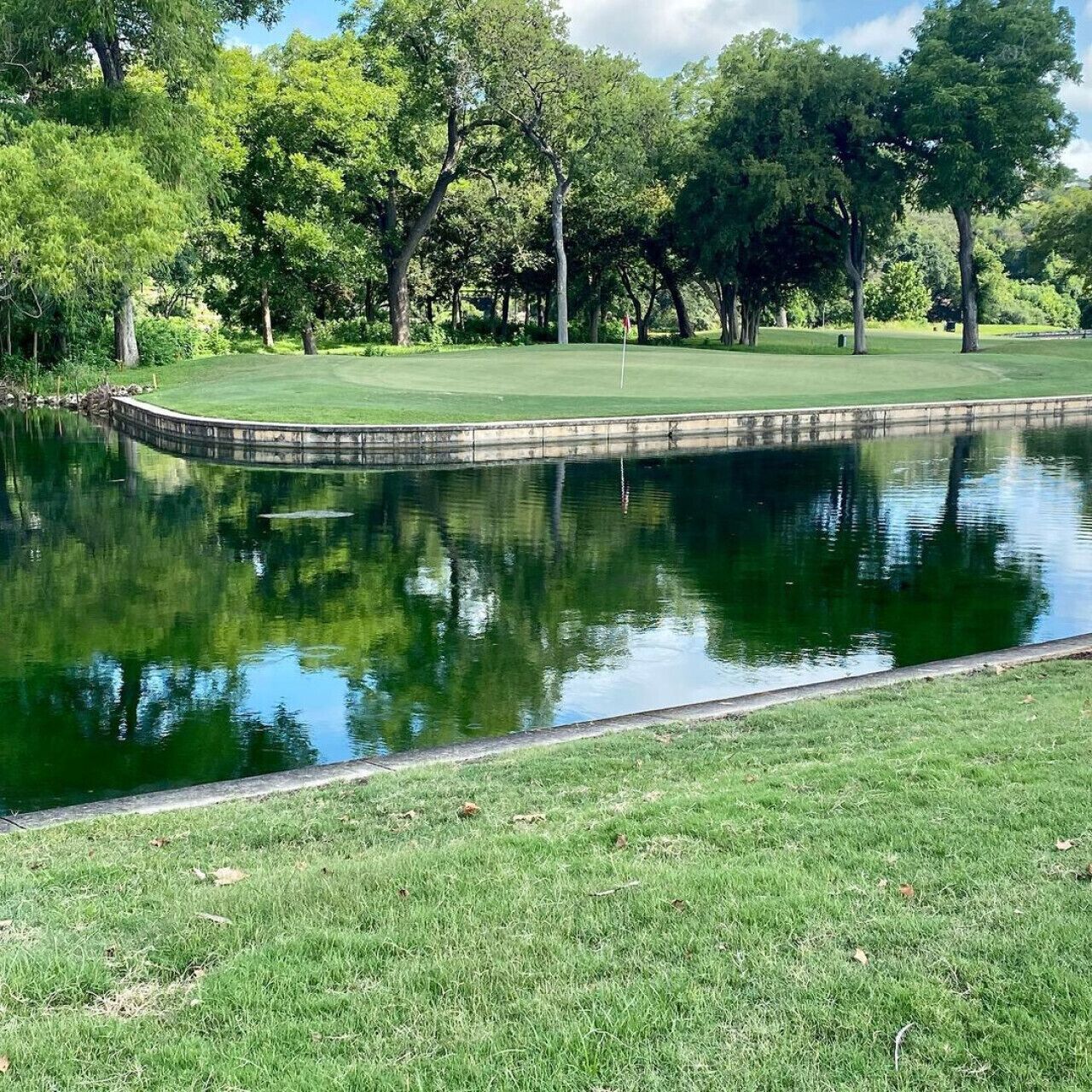 Ein friedlicher Golfplatz mit Teich, umgeben von üppigen Bäumen und einem gepflegten Rasen.