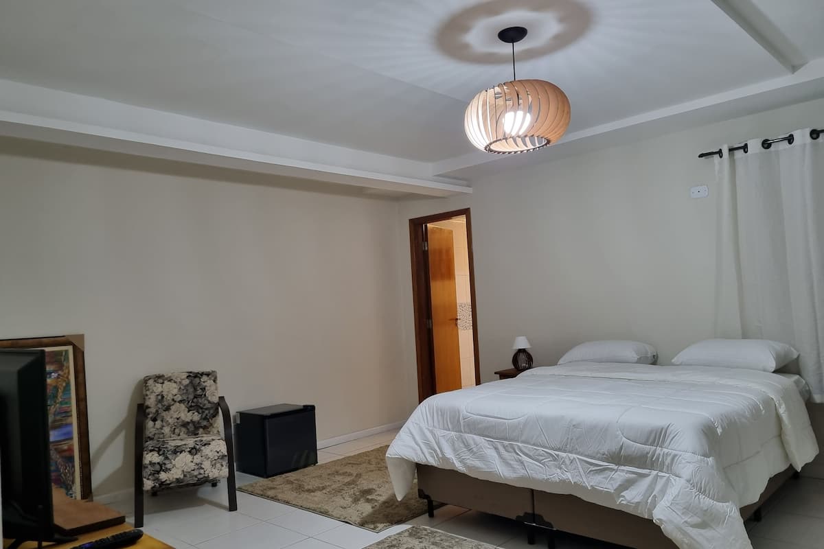 A bedroom with a bed, a TV, a remote, a lamp, and a door.