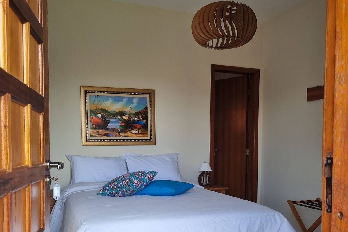 A bedroom with a bed, a painting, a wooden door, and a hanging light fixture.