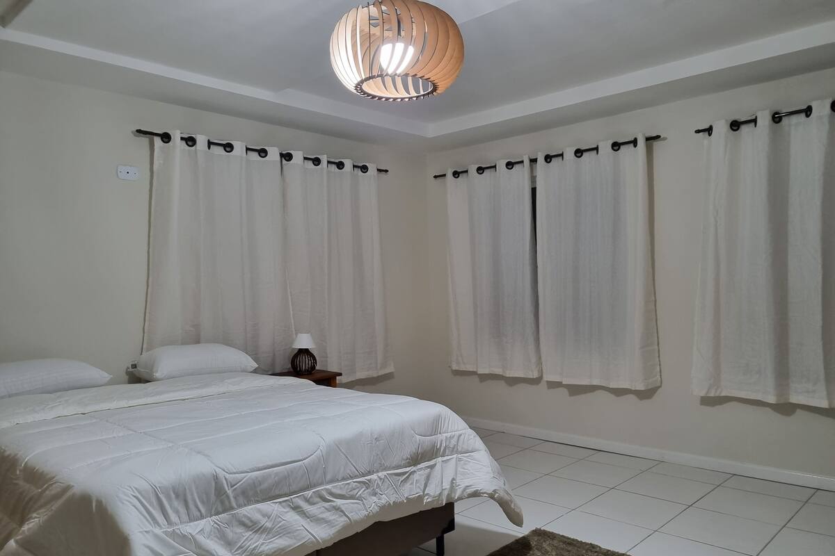 A bedroom with a bed, curtains, a nightstand, a lamp, and a ceiling light fixture.