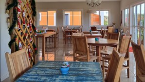 A spacious dining area with wooden tables and chairs, a decorative Christmas tree, and large windows providing natural light. - Pousada Caminhos da Vila Chantal (Campos do Jordão)