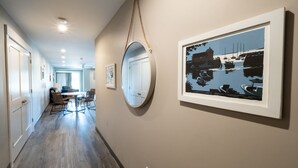 A hallway with a dining area, a round mirror, and a framed artwork of a marina.