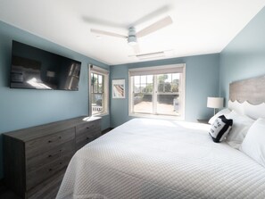 Ein Schlafzimmer mit Bett, Kommode, Deckenventilator, Fenstern und Kunstwerken.