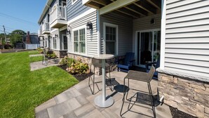 A two-story house with a covered patio area featuring outdoor seating and a stone wall.