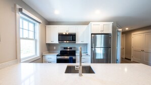 A modern kitchen with white cabinets, stainless steel appliances, and a large window.