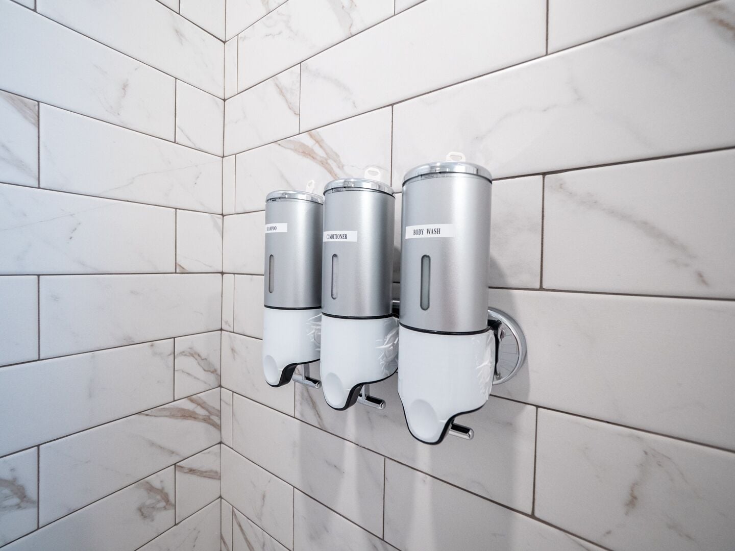 A bathroom with three wall-mounted dispensers labeled for hand soap, lotion, and body wash.