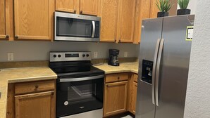 A kitchen with wooden cabinets, a stainless steel microwave, a stove, a refrigerator, and a coffee maker. - -Near Disney-  condo in gated Bahama Bay Resort (Davenport)
