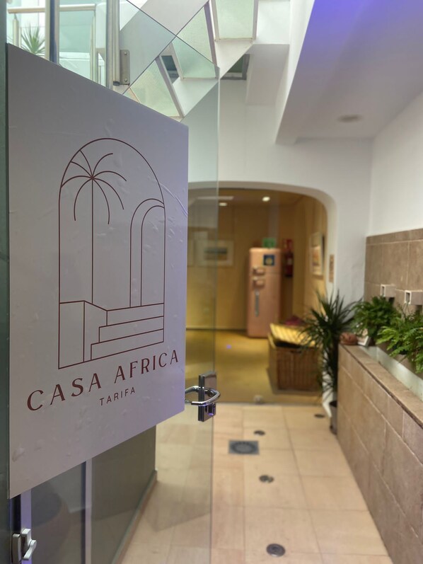 A modern hotel lobby with a glass partition displaying the logo 'CASA AFRICA TARIFA'.