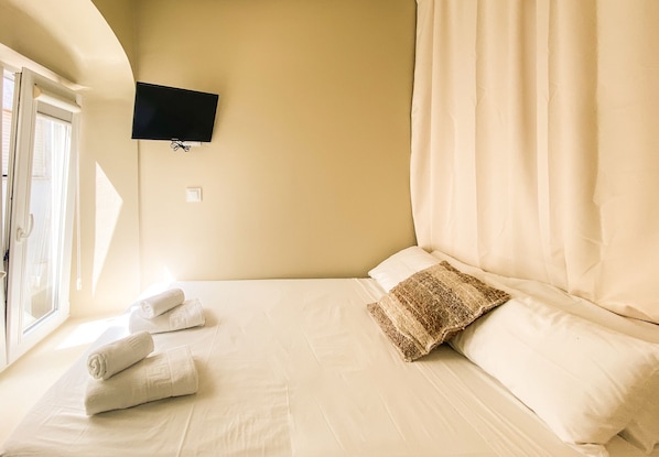 A neatly made bed with white linens, a patterned throw pillow, and rolled towels on the side. A flat-screen TV is mounted on the wall above the bed. - Casa Africa (Tarifa)