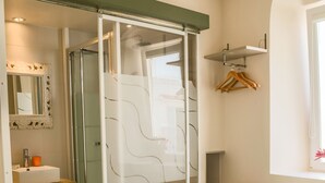 A modern bedroom with a glass-enclosed shower, a white bed with towels, a wooden vanity, and a mirror with a decorative frame. - Casa Africa (Tarifa)
