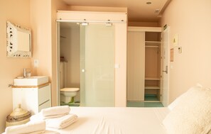 Una habitación de hotel con una cama, un baño con puerta de vidrio, un lavamanos y un espejo.