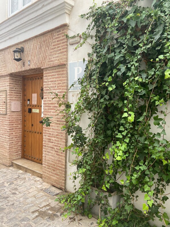 Un edificio de ladrillo con una puerta de madera, un cartel que indica una zona de estacionamiento y hiedra que crece en la pared.