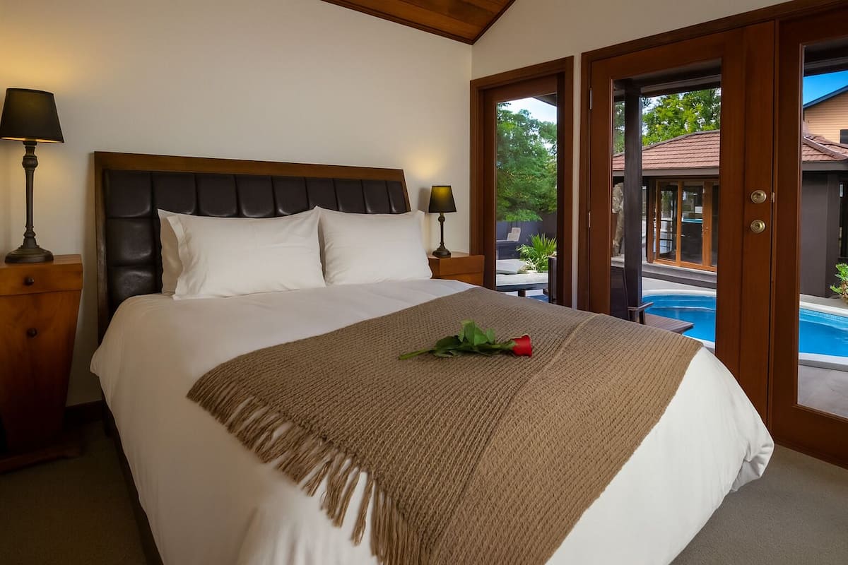A neatly made bed with a headboard, a bedside lamp, and a rose on the bedspread.