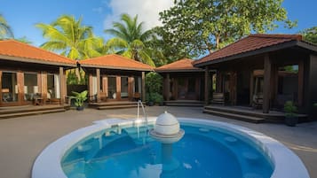 Une piscine avec une fontaine, entourée d’espaces de repos abrités et de palmiers.