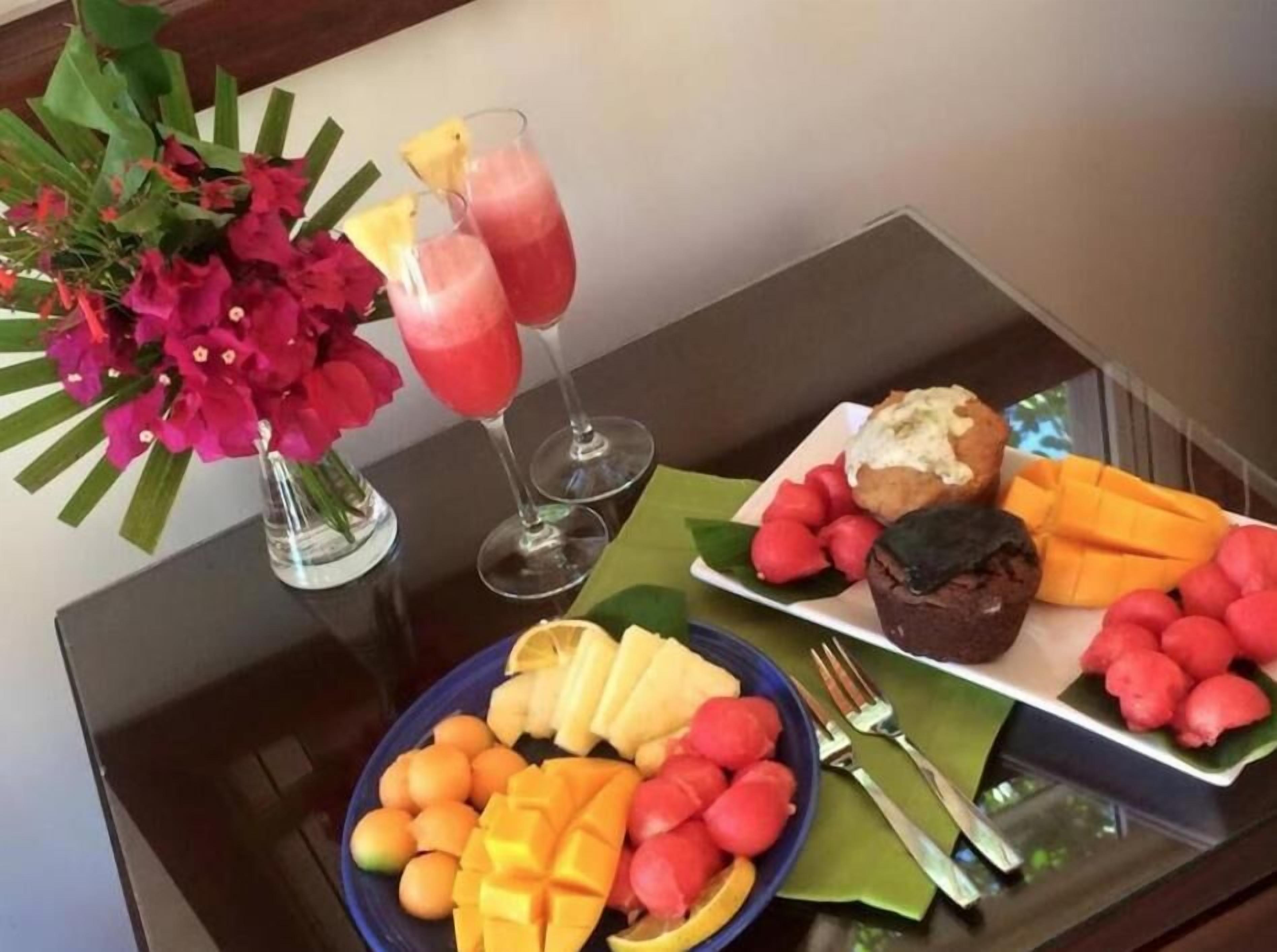 Una mesa con una bandeja de frutas, dos bebidas y un muffin.