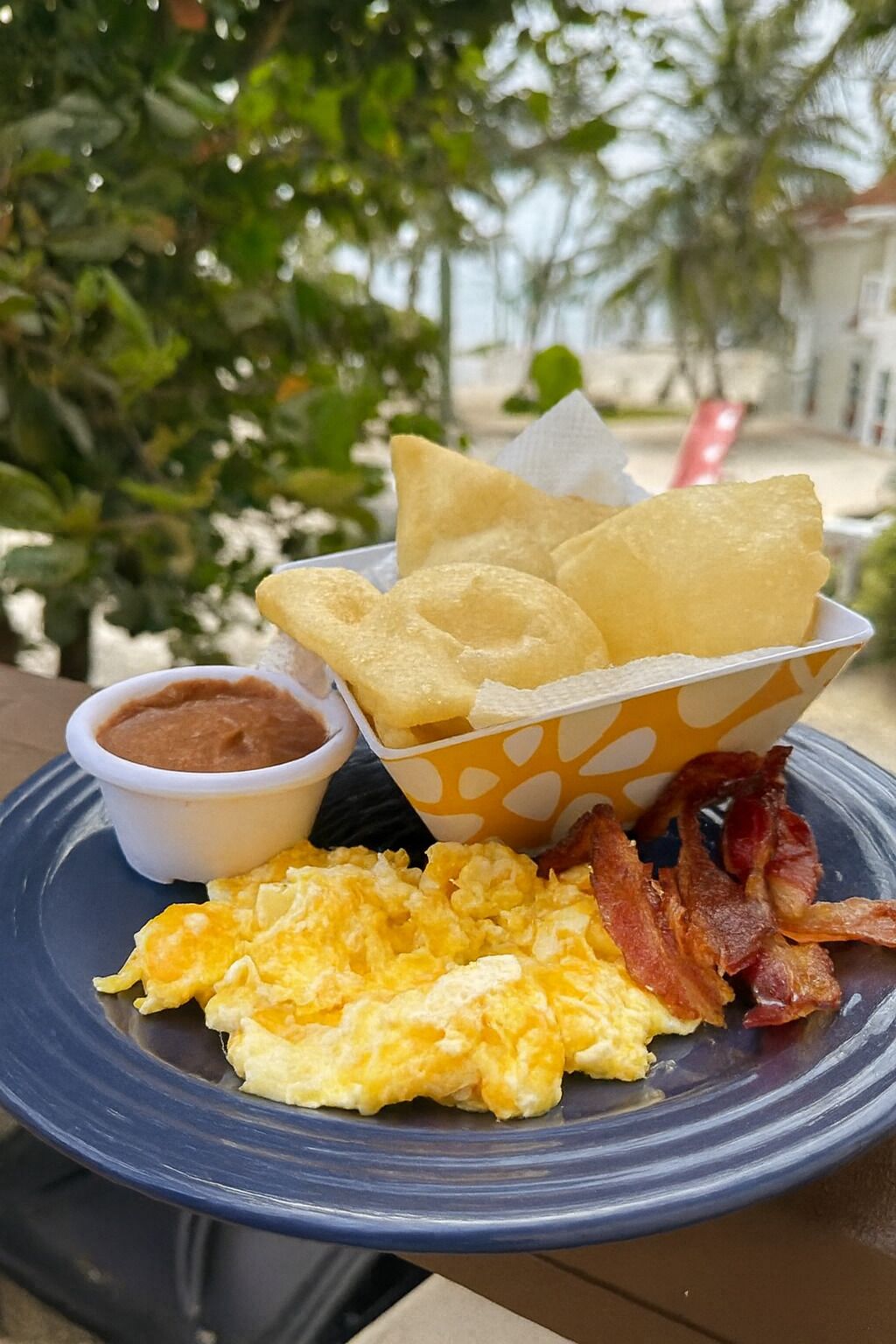 A plate with scrambled eggs, bacon, and a bowl of refried beans.
