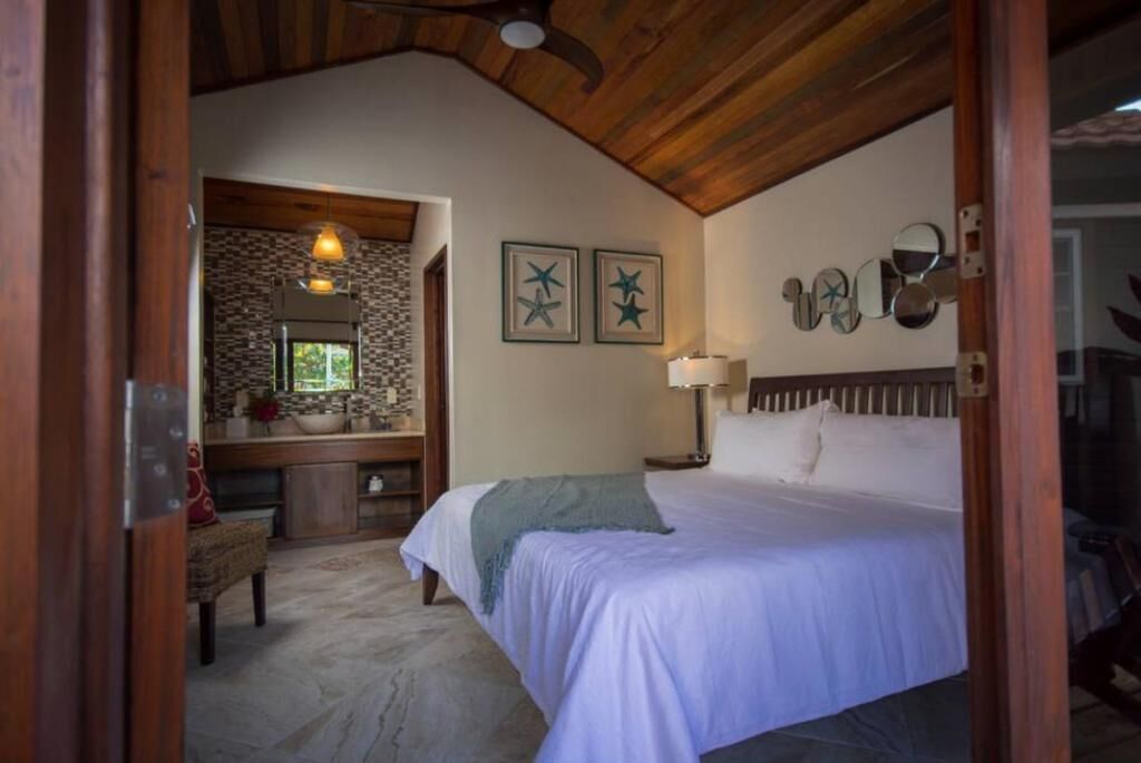 Un dormitorio con una cama grande, techo de madera, pared de piedra, baño con espejo y ventana.