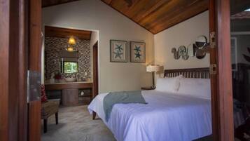 Un dormitorio con una cama grande, techo de madera, pared de piedra, baño con espejo y ventana.