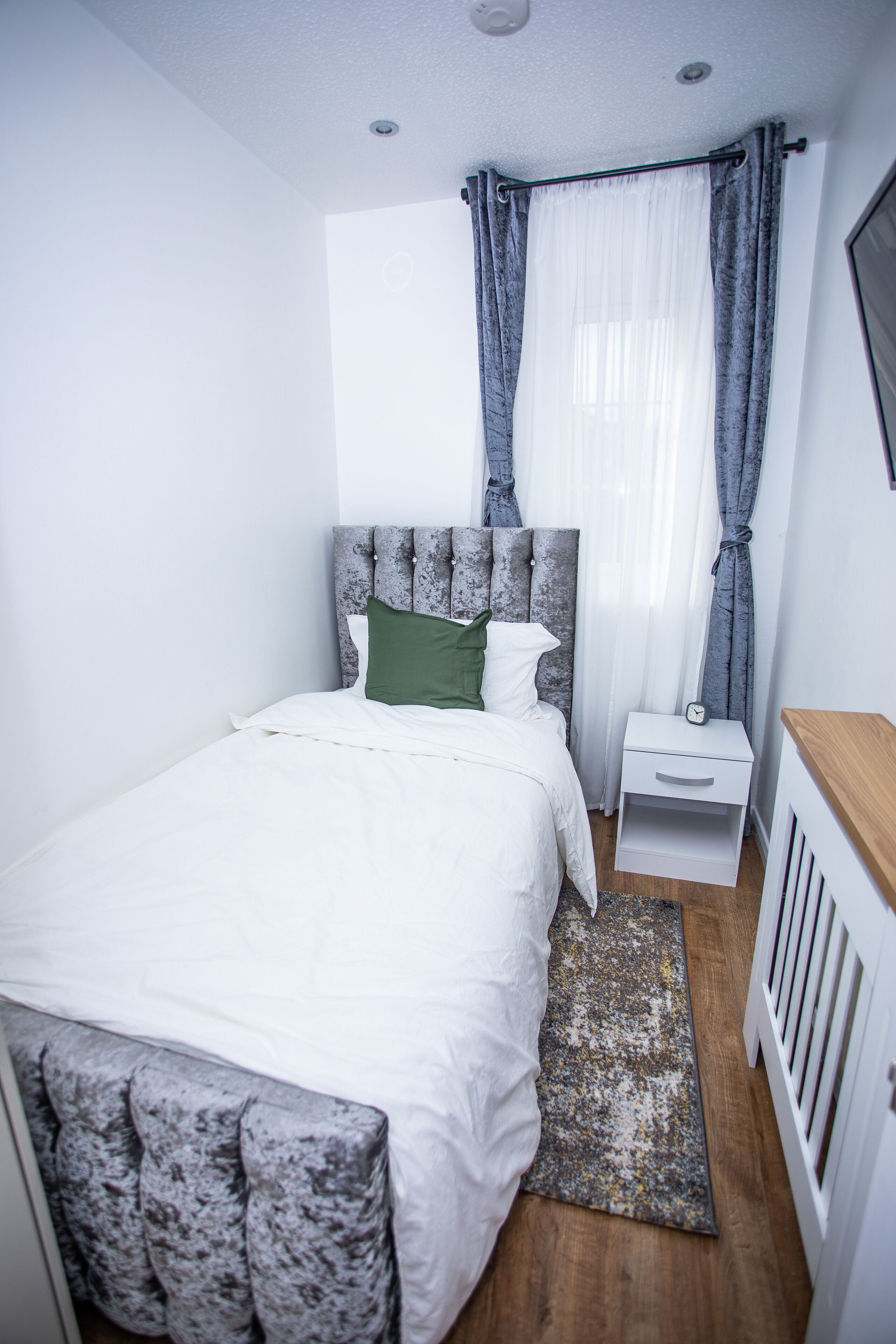 A bedroom with a bed, a nightstand, a wooden bench, and a radiator.