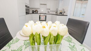 Una cocina moderna con armarios blancos, una mesa de comedor con un centro de mesa de tulipanes y sillas negras.