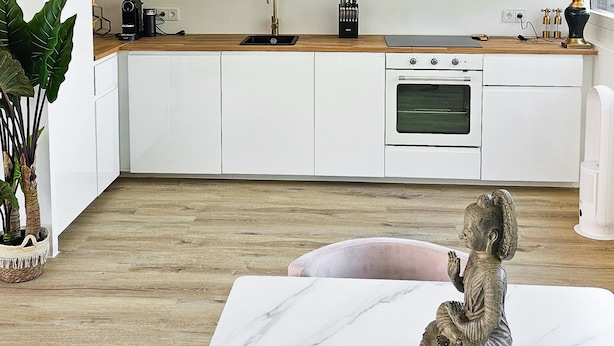A modern kitchen with white cabinets, a marble countertop, and a dining area with a table and chairs. - Luxus Dachgeschoss City Wohnung München (Munich)