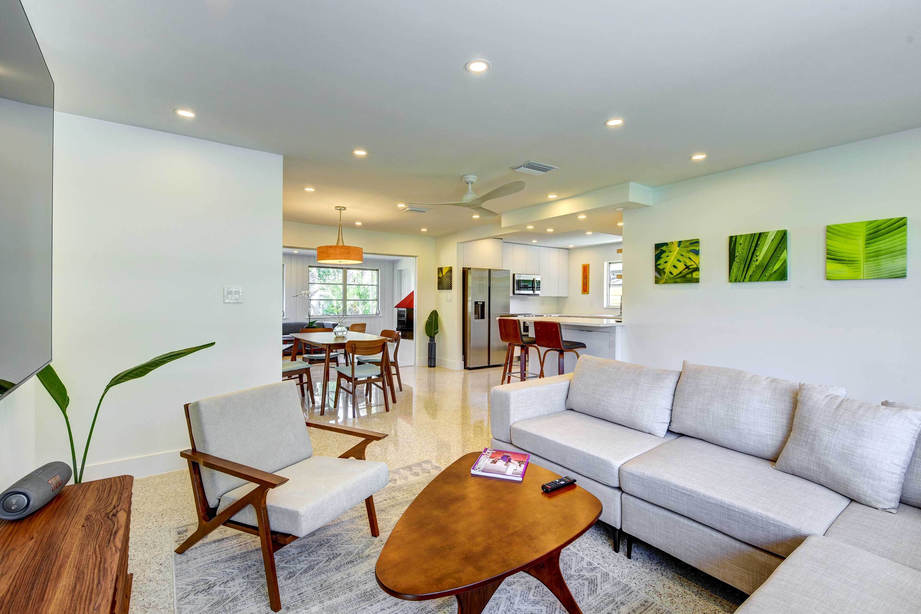 A modern living room with a sofa, armchairs, a coffee table, and a dining area with chairs and a table.