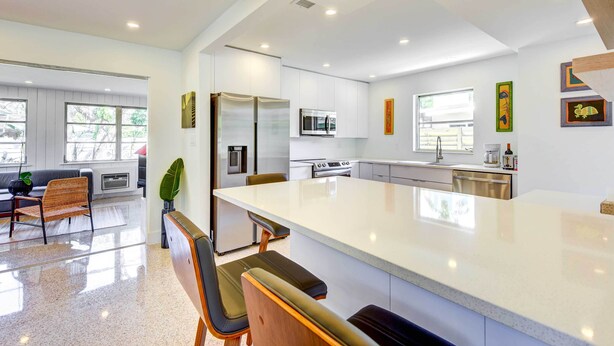Een moderne keuken met witte kastjes, roestvrijstalen apparatuur en een groot eiland met barkrukken.