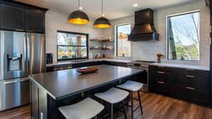 A modern kitchen with a large island, stainless steel appliances, dark cabinetry, and pendant lighting. - 3 Pines Lodges: Luxury, Mountain View, & Hot Tub! (Sevierville)
