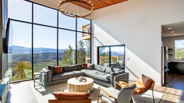 A spacious living area with large windows offering a mountain view, a modern chandelier, and a cozy seating arrangement. - 3 Pines Lodges: Luxury, Mountain View, & Hot Tub! (Sevierville)