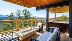A wooden deck with a fire pit, outdoor seating, and a hot tub overlooking a mountainous landscape. - 3 Pines Lodges: Luxury, Mountain View, & Hot Tub! (Sevierville)