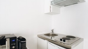 Een compacte keuken met een ingebouwde magnetron, een koffieapparaat, een spoelbak en een kookplaat.