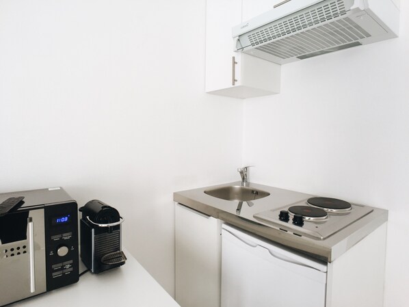 A compact kitchen with a built-in microwave, a coffee machine, a sink, and a stove. - Small Studio in Paris's 15th Convention/Vaugirard (Paris)