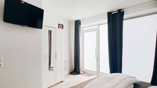 Een slaapkamer met een bed, een kledingkast, een televisie en een schuifdeur naar buiten.