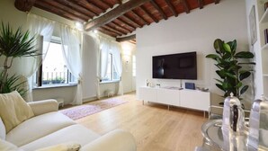 A living room with a white sofa, a flat-screen TV, a white cabinet, and a large window with curtains. - Corte Paolina - charming courtyard inside Lucca (Lucca)