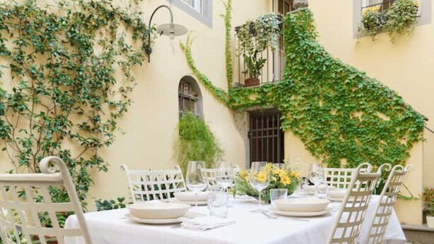 An outdoor dining area with a table set for four, surrounded by white chairs, and covered with a white tablecloth. - Corte Paolina - charming courtyard inside Lucca (Lucca)