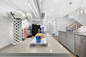 A modern kitchen with a stainless steel countertop, a white vase with white flowers, and a tray with blue cups.