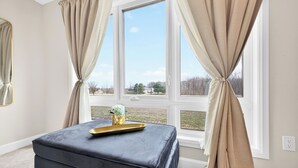 A room with a large window, a black ottoman, and a gold tray on the ottoman.