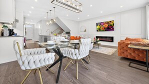 A modern kitchen with white cabinetry, a dining area with a glass table, and a living room with a fireplace.