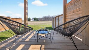 A wooden deck with two wicker chairs and a small round table with two glasses.