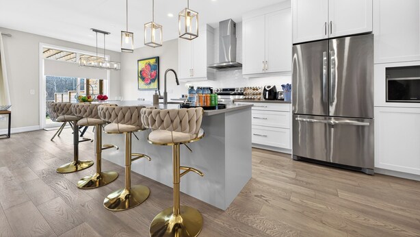 A modern kitchen with white cabinets, stainless steel appliances, and gold bar stools.