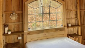 A wooden cabin room with a bed, a window, and a shelf with plants. - STARWOOD - PET FRIENDLY! - OFF GRID - ROMANTIC - ON WINE TRAIL (Hammondsport)